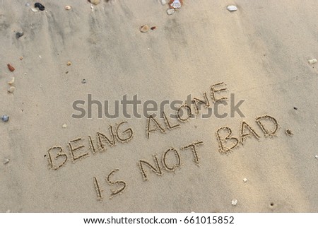 Handwriting  words "BEING ALONE IS NOT BAD." on sand of beach.