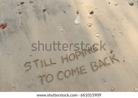 Handwriting  words "STILL HOPING TO COME BACK on sand of beach.