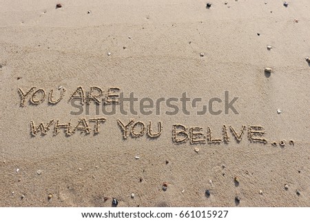 Handwriting  words "YOU ARE WHAT YOU BE LIVE." on sand of beach.