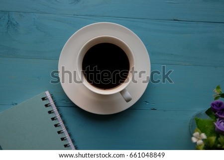 Black coffee , violet flowers and diarybook on blue wooden table. Picture  that select focus and copy space that  have flare light