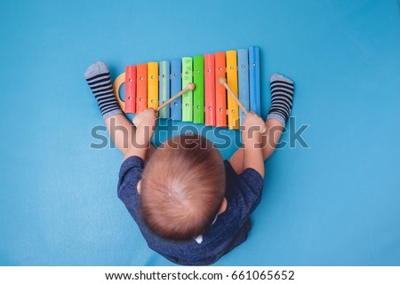 Bird eye view of Cute little Asian 18 months / 1 year old baby boy child hold sticks & plays a musical instrument colorful wooden toy xylophone, Educational toy for kids and toddlers concept  Royalty-Free Stock Photo #661065652