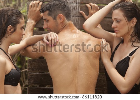 Two young girls and a handsome man taking a shower at the beach.