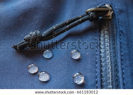 large rain drops dew on dark waterproof weatherproof membrane clothes. closeup macro shot of buckle, zipper, sealed pocket, fastener Royalty-Free Stock Photo #661183012