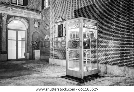 Vintage phone cabin at night street of Amsterdam. Black-white photo.