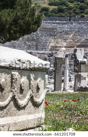 A white marble sarcophagus is on the grass. On the background the famous amphitheater of Ephesus is visible.