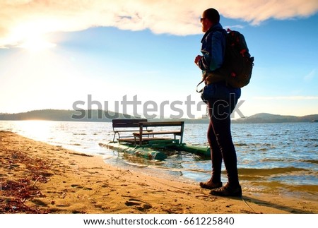 Tall tourist with backpack walk on beach at paddle boat in the sunset. Autumn at se.