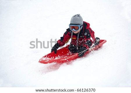 A young boy shows his excitement sledding down a hill in winter.