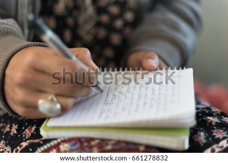 Close up of a woman's hands writing with a pen on a notepad.