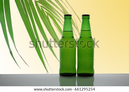  In the picture there are two beer bottles , palm leaf,Green leaves,orange light ,And Some palm leaves are out of focus.