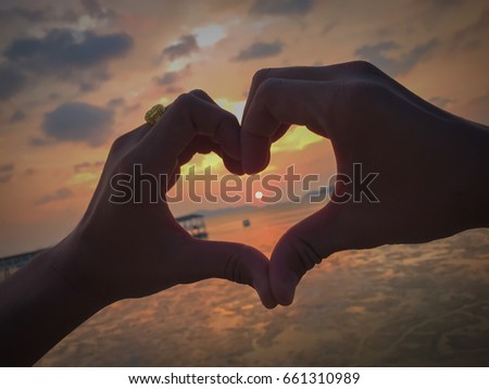 Shape of heart done with silhouette of hands on a beach with sunset sun and colors - Symbol of love - Concept about romantic travels, summer, valentine, honeymoon.