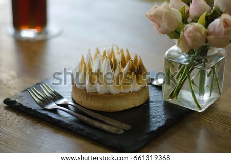Signature dish. French pastry Lemon Meringue Tart on rustic black plate with flower vase, signature dessert in cafe