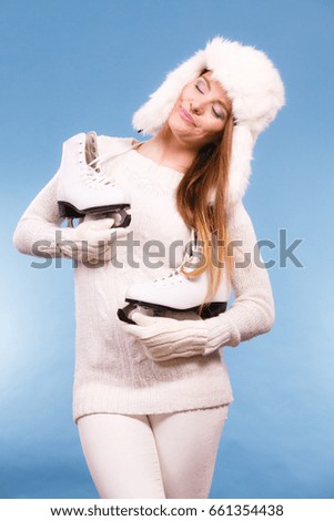 Woman with ice skates getting ready for ice skating. Winter sport activity. Smiling girl wearing warm clothing sweater and fur cap on blue studio shot