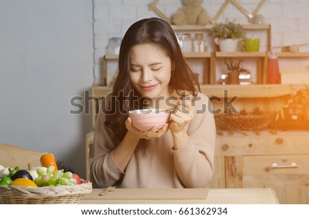 Happy young woman eating soup in kitchen