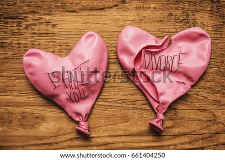 couple of deflated pink red balloon with the words: i hate you and divorce lie on wooden table background. two rubber broken balloon