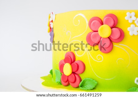 Colorful children's birthday cake made of yellow mastic decorated with pink flowers, leaves, pattern on a white background. Close-up. Cutout. Picture for a menu or a confectionery catalog.