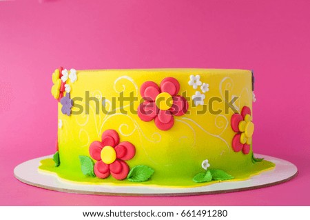 Colorful children's birthday cake made of yellow mastic decorated with pink flowers, leaves, pattern on a pink background. Cutout. Picture for a menu or a confectionery catalog.