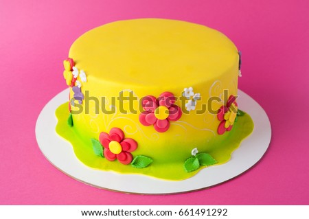 Colorful children's birthday cake made of yellow mastic decorated with pink flowers, leaves, pattern on a pink background. Close-up. Cutout. Picture for a menu or a confectionery catalog.