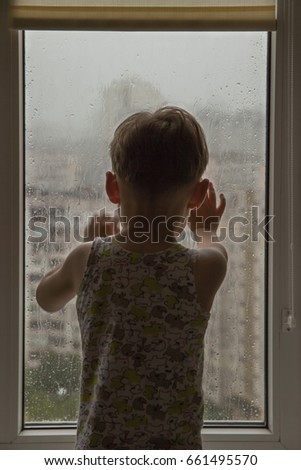 Silhouette of a little boy standing by window with raindrops on a rainy day