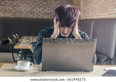 Portrait of an upset businessman at desk in cafe. Businessman being depressed by working in cafe. Strain,Yong business man to think and not Work with stress Pretending to put his hand to the head.