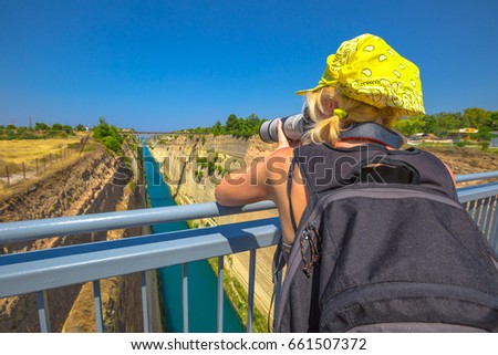 Travel photographer with telelens takes photos from Bridge of Corinth Channel. Corinth Canal connects the Gulf of Corinth with the Saronic Gulf in Aegean Sea. Female photographer in Greece, Europe.
