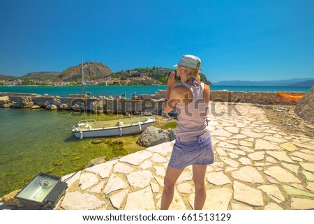 Travel woman photographer takes shot of Nafplio, famous seaside town of Peloponnese, Greece from Fortaleza de Bourtzi. Female photographing Palamidi Fortress a top of mountain. Travel vacation concept