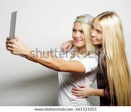 two hipster girls friends taking selfie with digital tablet, studio shot over gray vackground