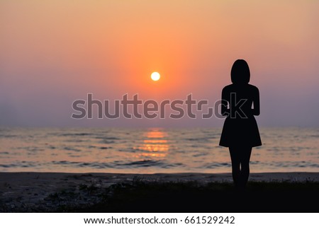 Silhouette of a woman standing by the sea and the sunset