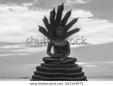 Buddha and many headed serpent, at a Thai temple, with sunset sky background.
