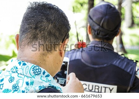 the tourist taking picture guard security with mobile phone from behind
