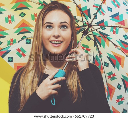 Happy young woman holding an umbrella on a yellow background