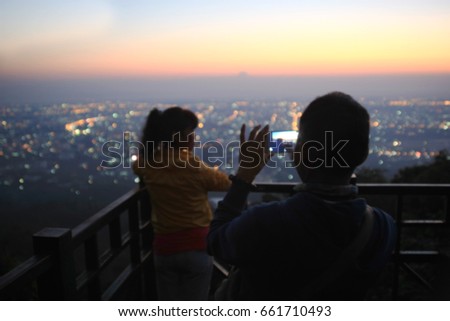 Blurred Asian men use mobile phones to take pictures of lovers in the evening. With bokeh lighting as background.