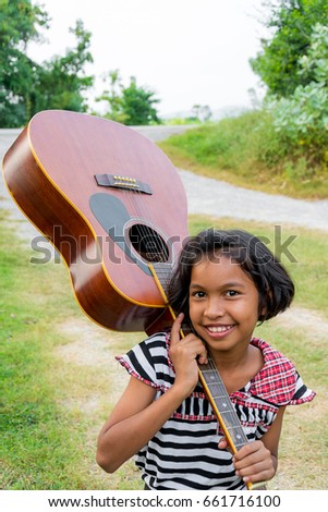 Little girl posing with guitar and smile on field
