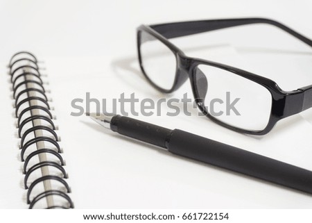 Eye glasses, black pen and notepad on a white background.