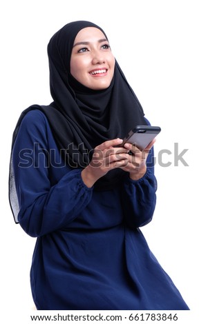 Young Asian Muslim woman in head scarf smile with smartphone and holding book. Royalty-Free Stock Photo #661783846