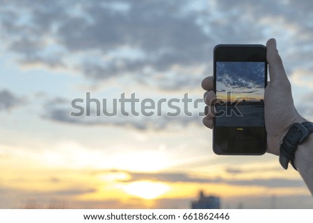 Man taking photos of sunset with smartphone camera on summer colorful evening.