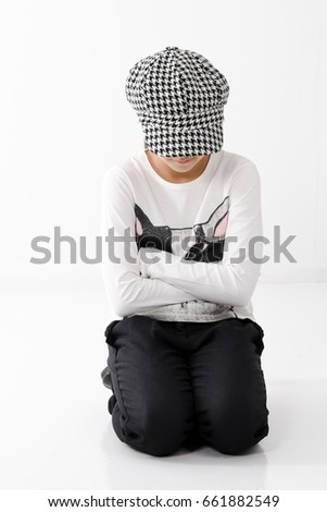 Autumn fashion for girls. Teenage clothing. The girl sits on her lap and covers herself with her cap. On a white background
