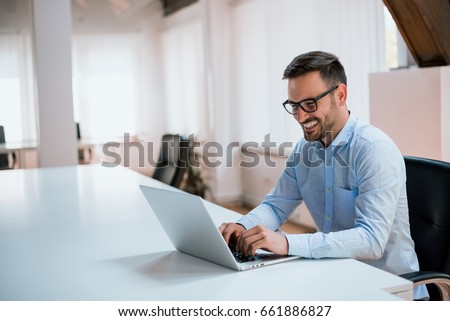 Happy young businessman using laptop at his office desk. Royalty-Free Stock Photo #661886827