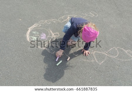 the baby girl draws on the pavement with crayons thinking about mom.