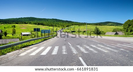 Rural road and zebra crossing, green hills on background in sunny day