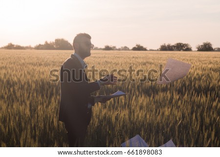 Portrait of young businessman throwing sheets of paper into the air, sunset in summer fields background