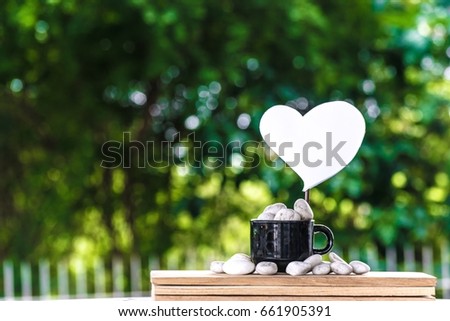 Cut a heart paper on a coffee mug on a wooden board and a Bokeh tree backdrop.