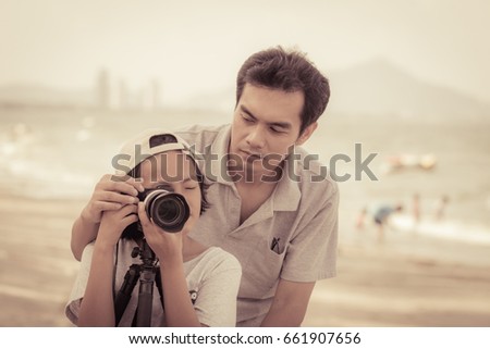 Dad is teaching daughter to take pictures on the beach on a summer holiday with vintage color tone
