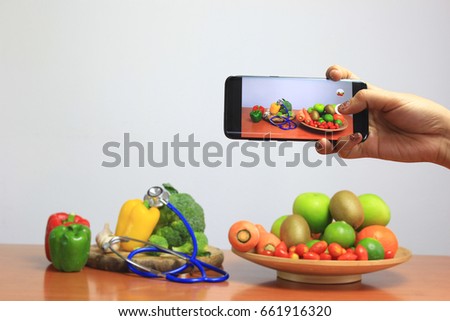 Woman using a smart phone to take a photo of Assortment of fresh fruits and vegetables on wooden table