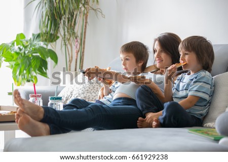 Happy young family, pregnant mother and two boys, eating tasty pizza at home, sitting on the sofa, watching TV and having a laugh Royalty-Free Stock Photo #661929238