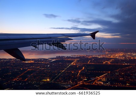 Wing view of civil passenger aiplane taking off at dusk with night city lights seen below. Royalty-Free Stock Photo #661936525