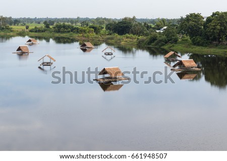 Scenic view of a lake with bamboo rafts, many vetiver roofs floating on the water near the tree garden on the shore.
