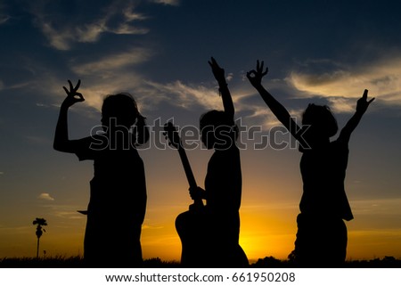 Silhouette,Group of happy children playing on meadow,holding on hands and hands up together in evening
