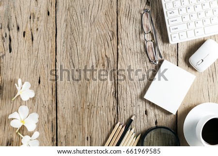 business objects of keyboard,mouse,white coffee cup,white paper,pencils,glasses,magnifying glass and frangipani flowers on old wooden table background