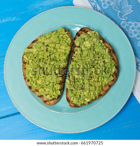 Two slices of avocado toast on a blue plate on, a painted blue wood background.
