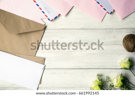 Top view of envelope and blank greeting card with rose flowers on white wooden background.